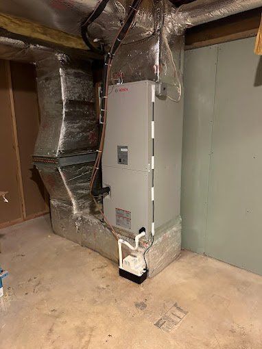 HVAC unit with ductwork in a basement setting. The unit is gray and silver with a white pipe.