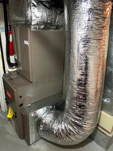 Furnace with silver ductwork in a basement setting.