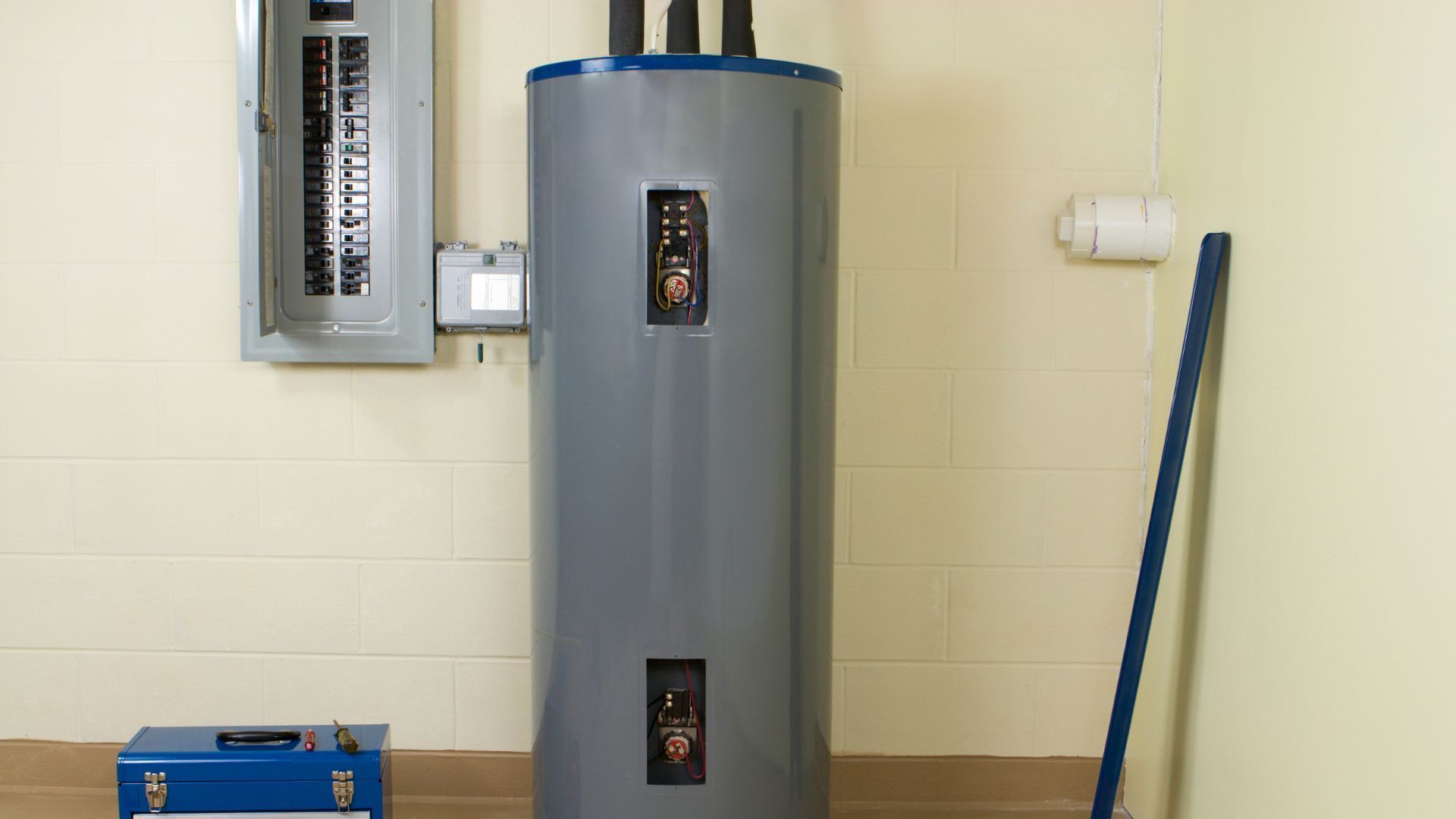 Electric water heater in a utility room next to an electrical panel and a toolbox.