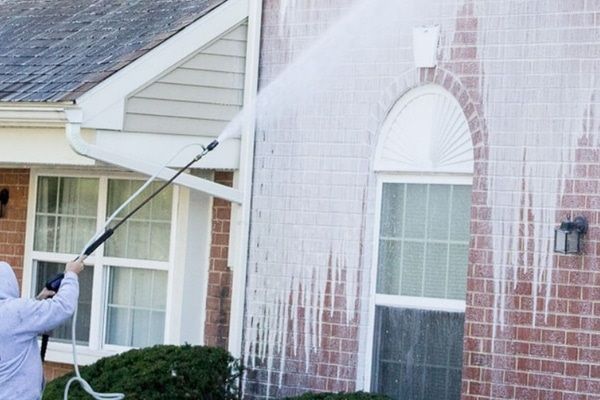 A man is cleaning the side of a brick house with a high pressure washer.