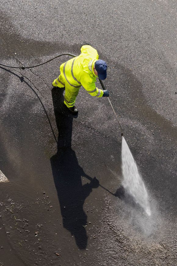 A man in a yellow jacket is using a high pressure washer to clean the ground.