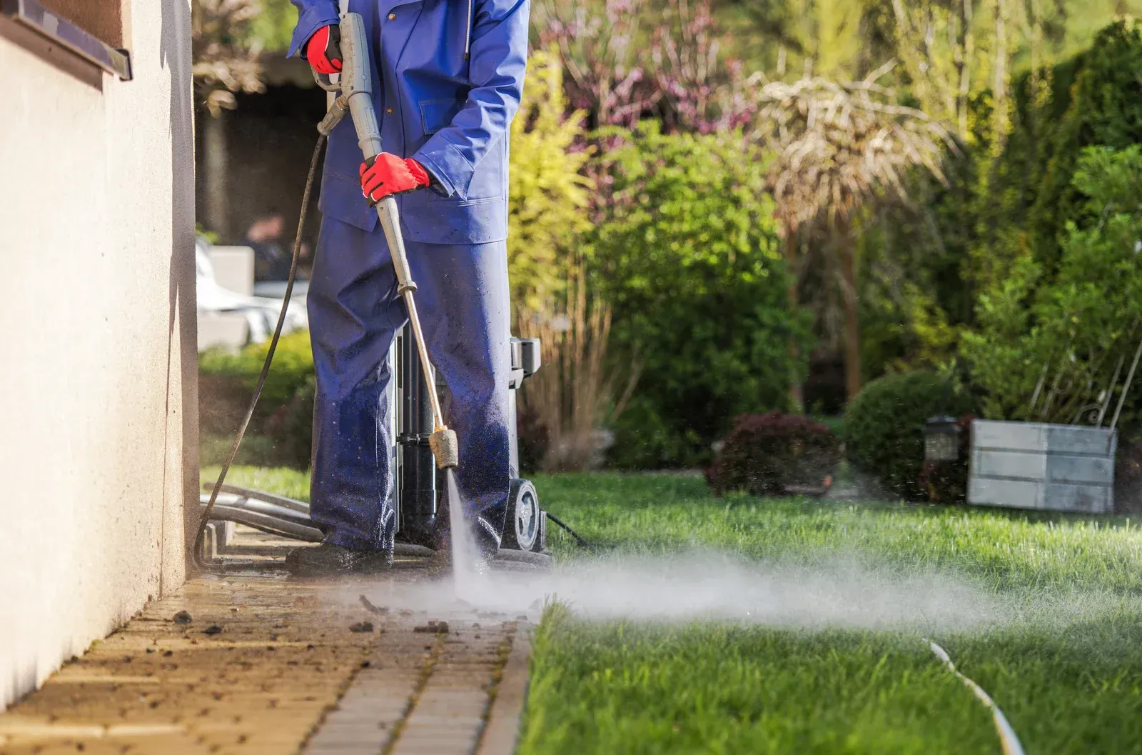 A man is using a high pressure washer to clean a sidewalk.