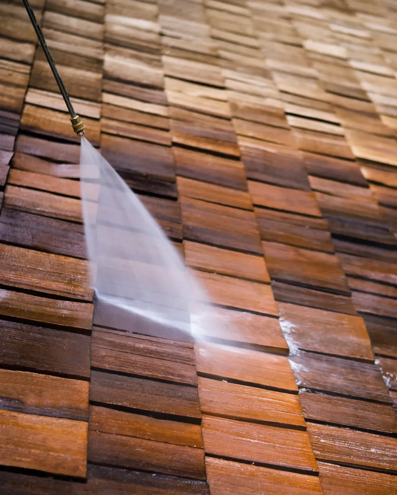 A person is cleaning a wooden roof with a high pressure washer.