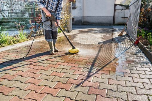 A man is using a high pressure washer to clean a brick driveway.