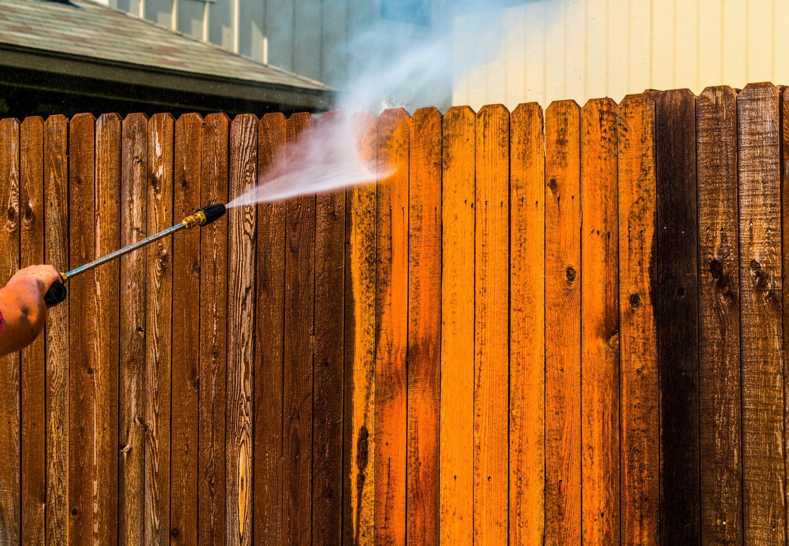 A person is cleaning a wooden fence with a high pressure washer.