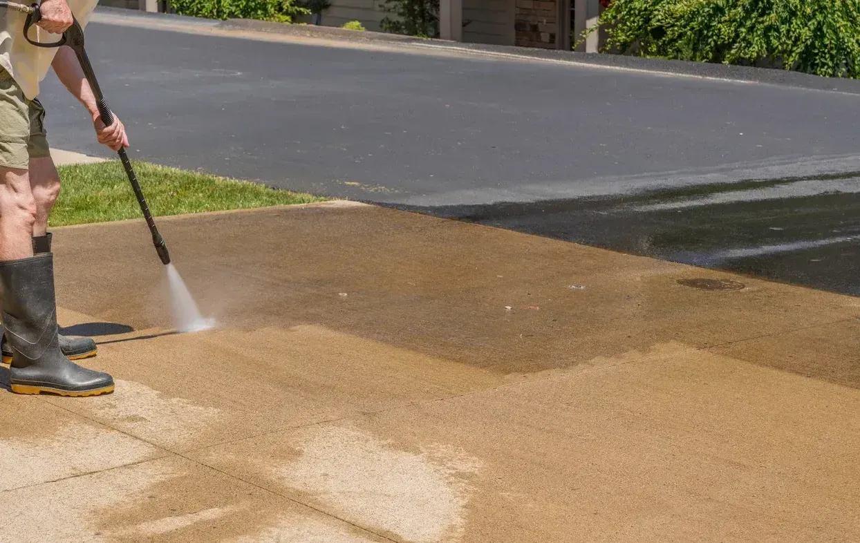 A man is using a high pressure washer to clean a sidewalk.