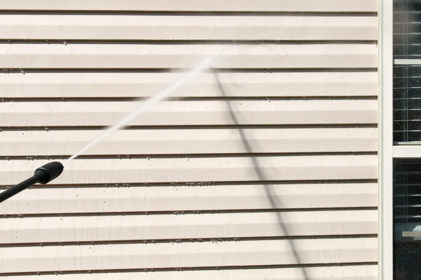 A person is using a high pressure washer to clean the side of a house.