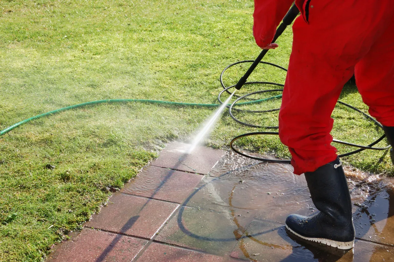 A person is using a high pressure washer to clean a sidewalk.