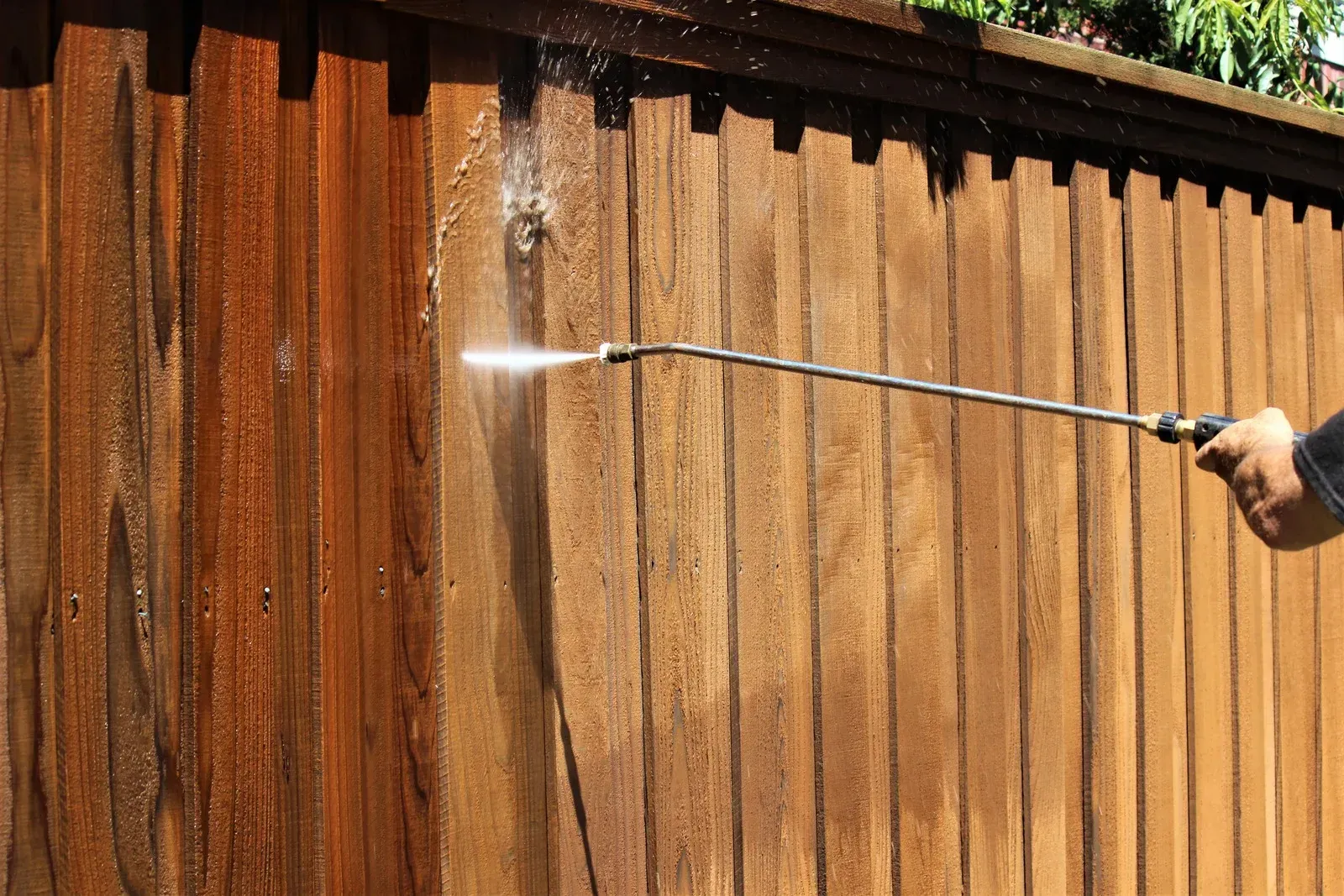 A person is cleaning a wooden fence with a high pressure washer.