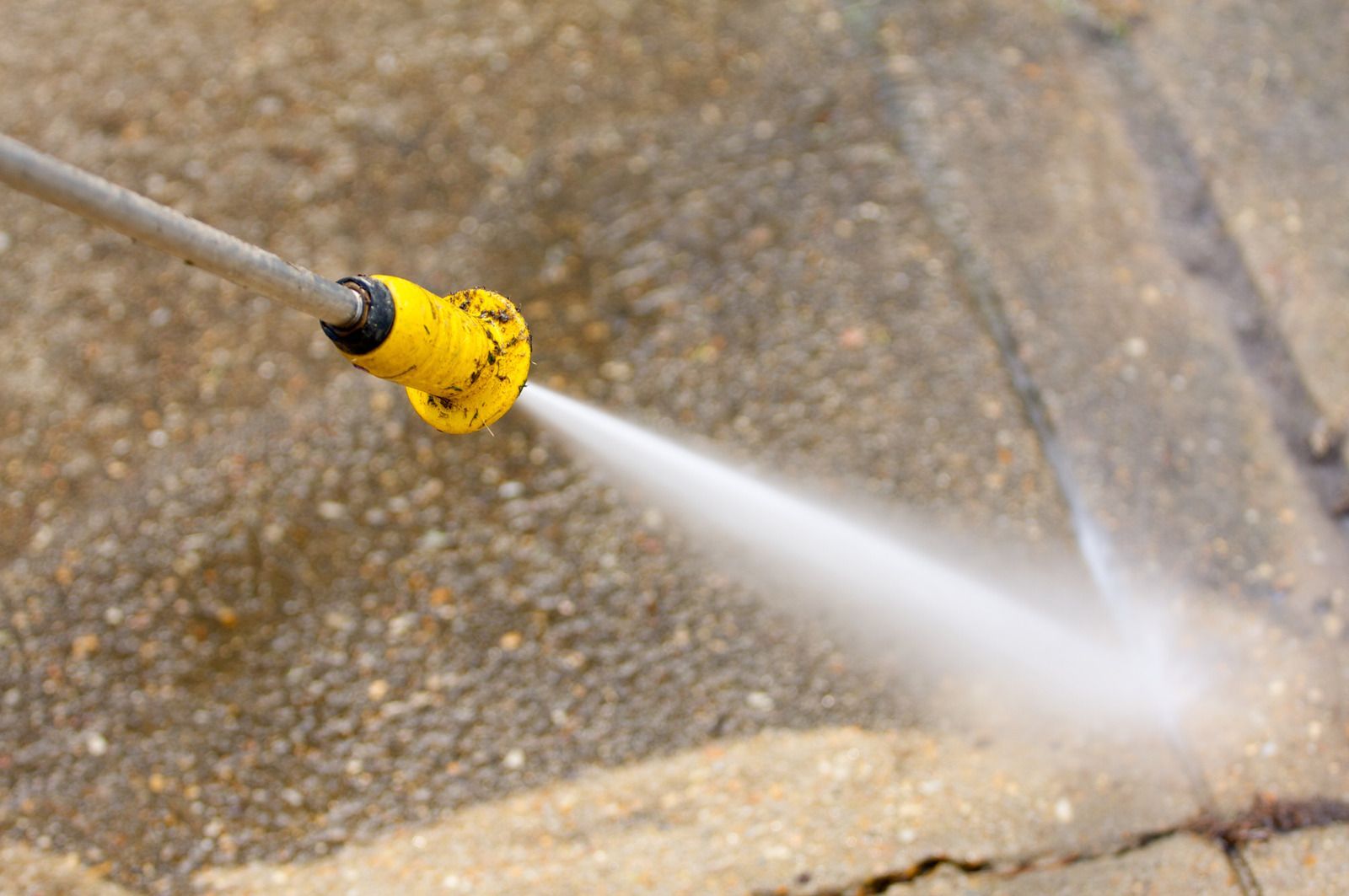 A person is using a high pressure washer to clean a brick sidewalk.