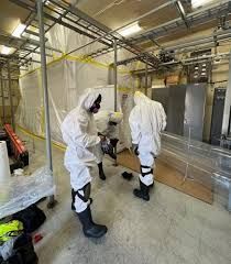 Two people in white hazmat suits vacuuming a laboratory floor.