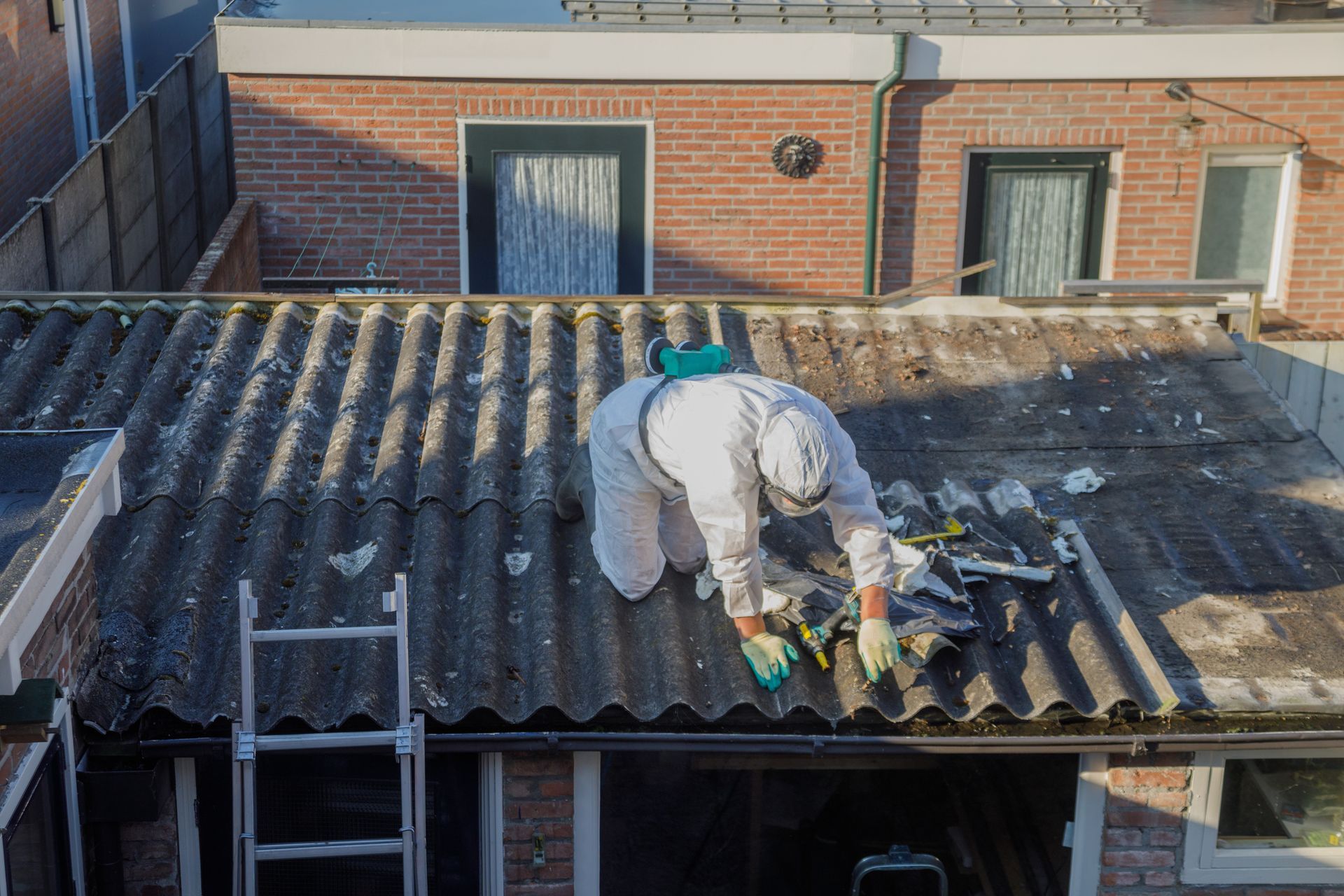 Two workers in protective suits removing siding from a house.