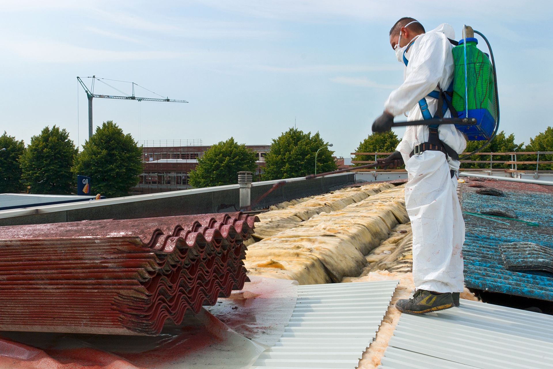 Person in protective suit spraying a roof, possibly for pest control. Green backpack sprayer, construction site.