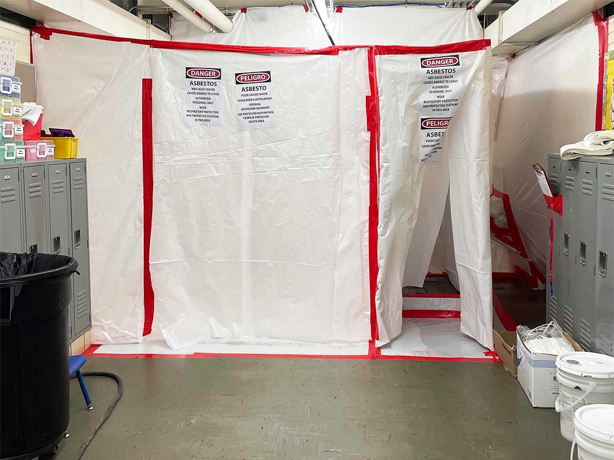 Person in protective suit inspecting a damaged asbestos roof on scaffolding, inside a building.