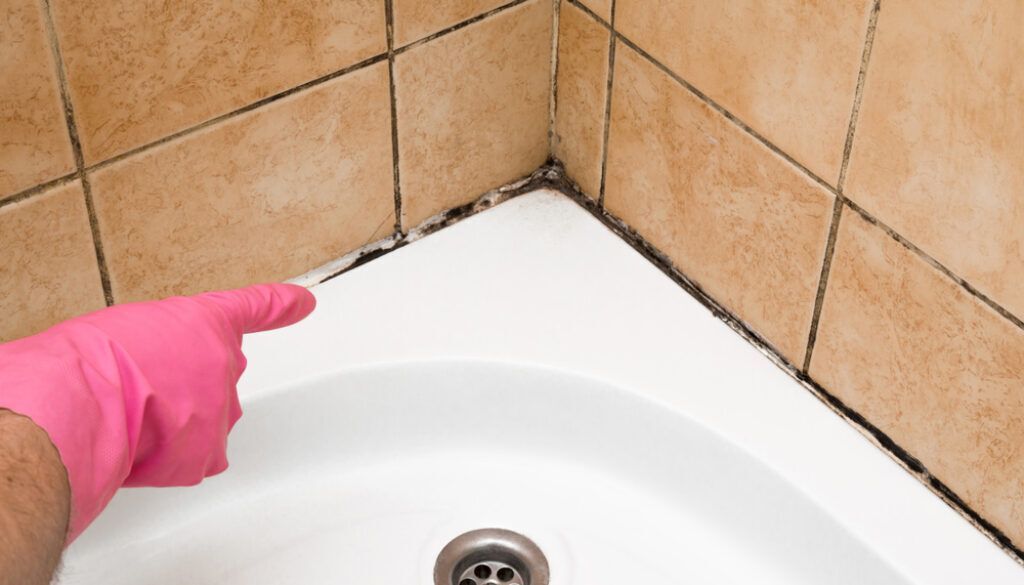 Person in protective suit cleaning a window on a house with blue siding.