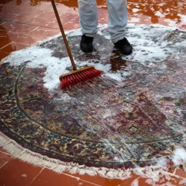 A person is cleaning a rug with a broom