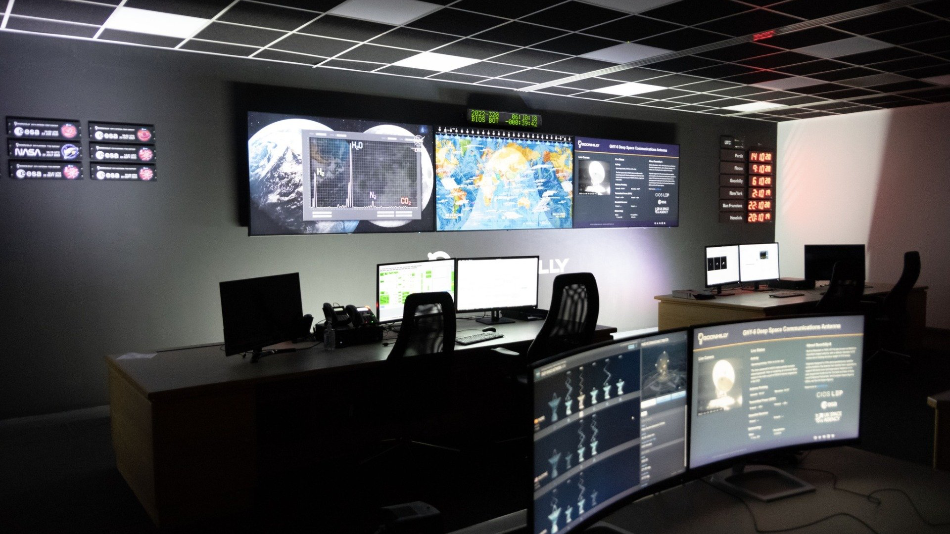 A picture of Goonhilly's Operational Control Centre (OCA) - the area in which the Deep Space Network Operations Team work. Large screens display information about lunar and deep space missions and computer stations are lit dramatically.