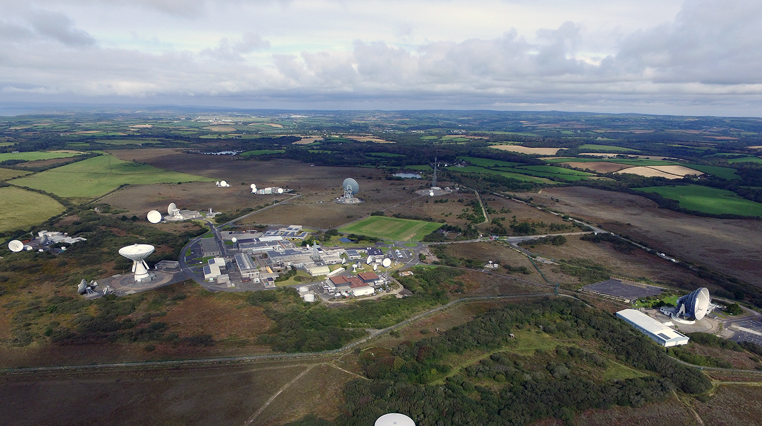 An aerial view of the Goonhilly Site shows a range of antennas communicating with LEO, MEO, and GEO satellites. Also shown are 3 dishes over 27m in diameter, the site's buildings and the surrounding natural area.