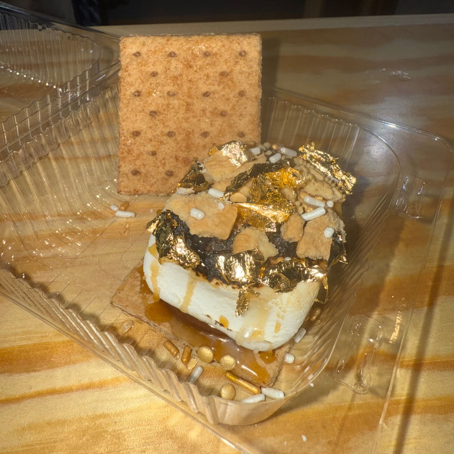 Marshmallow dessert topped with chocolate and crushed nuts in a clear plastic tray, with a cracker behind it