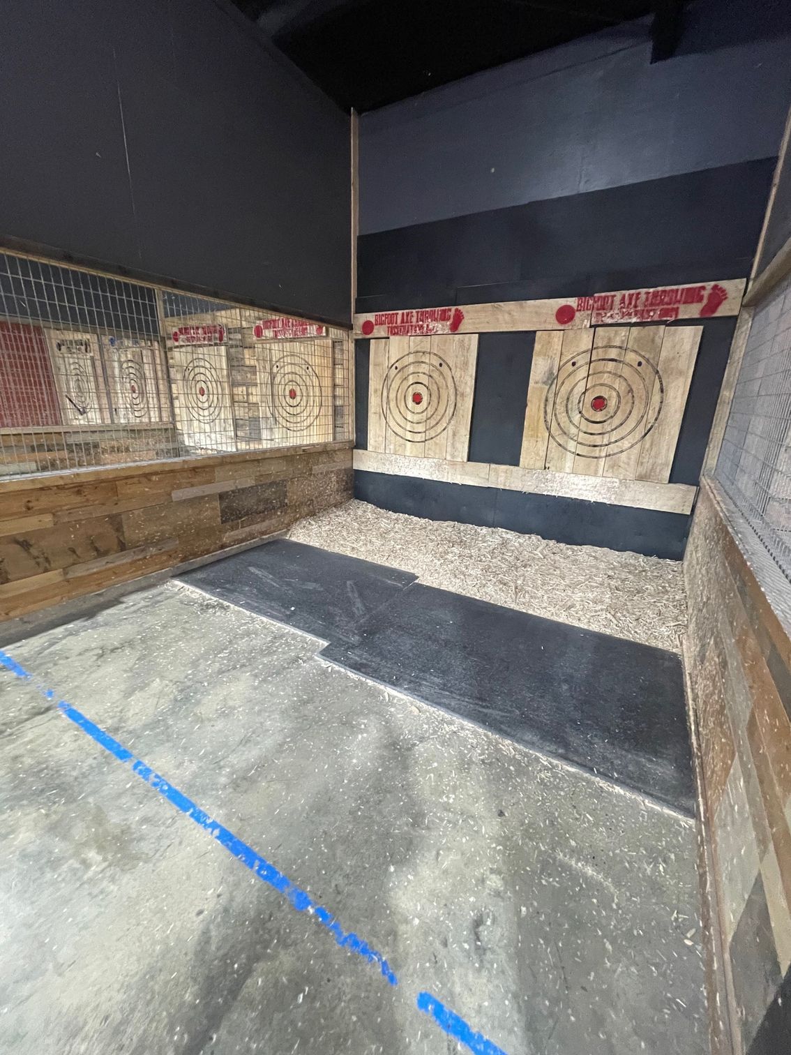 Indoor archery lane with target butts, concrete floor, and blue tape marking the shooting line.