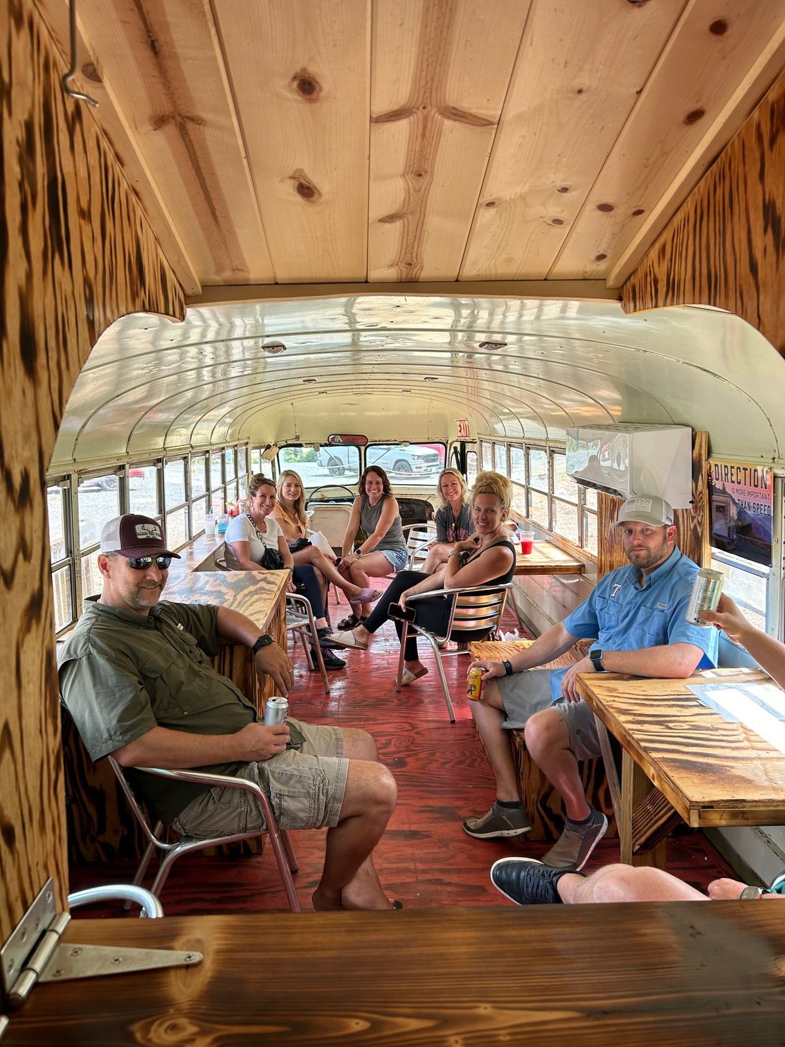 People seated inside a wood-paneled van, riding together and chatting on a bench seat.