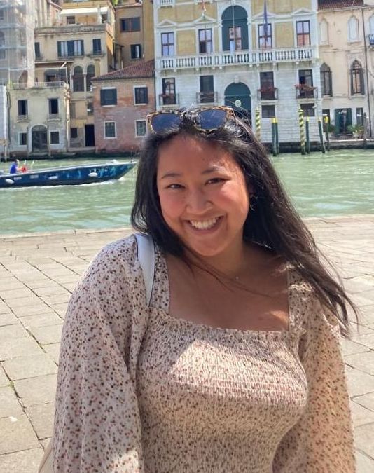 A woman wearing a white sweater and a black shirt is smiling with her arms crossed.