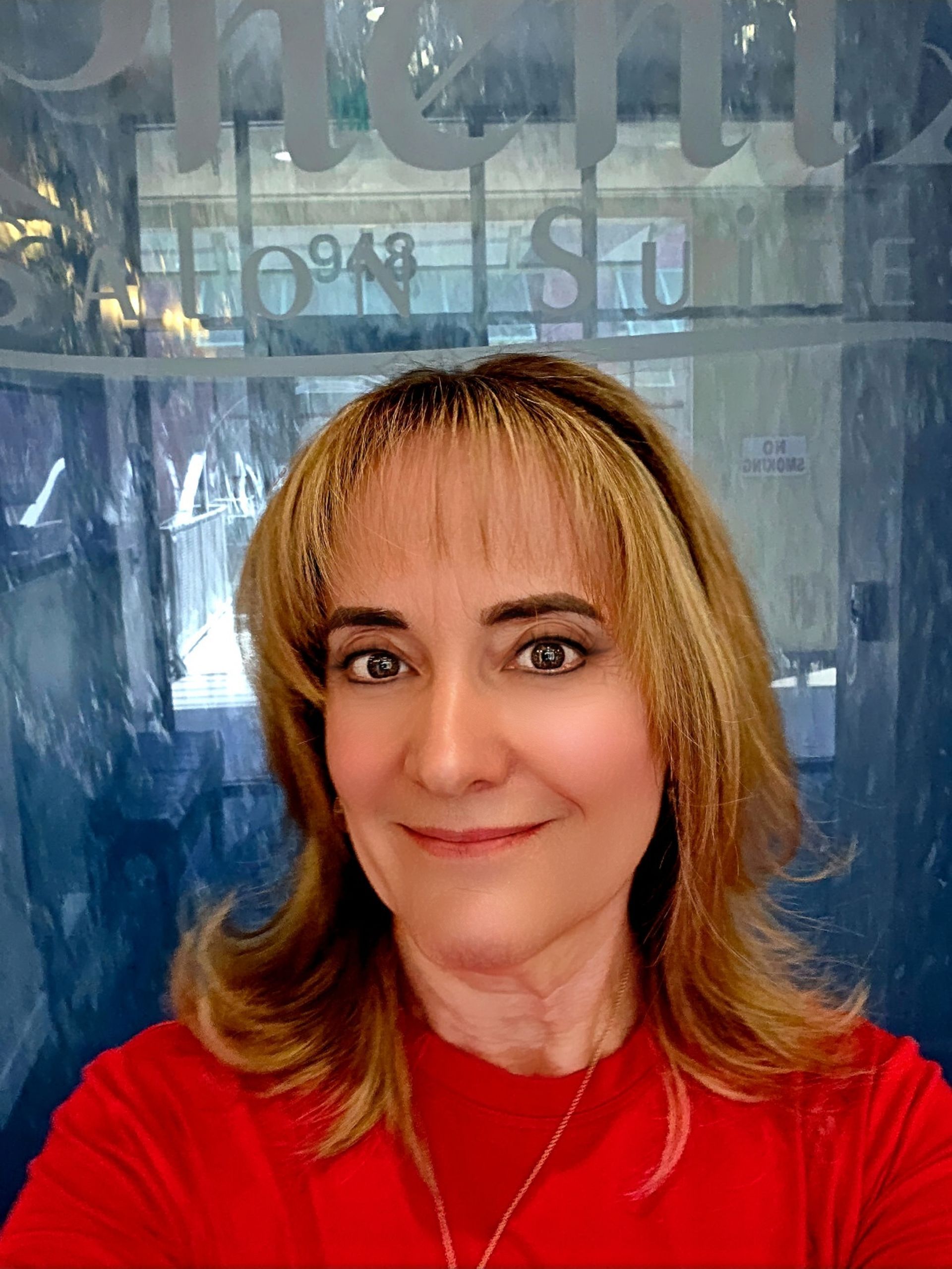 A woman in a sweater is smiling for the camera in front of a bush.