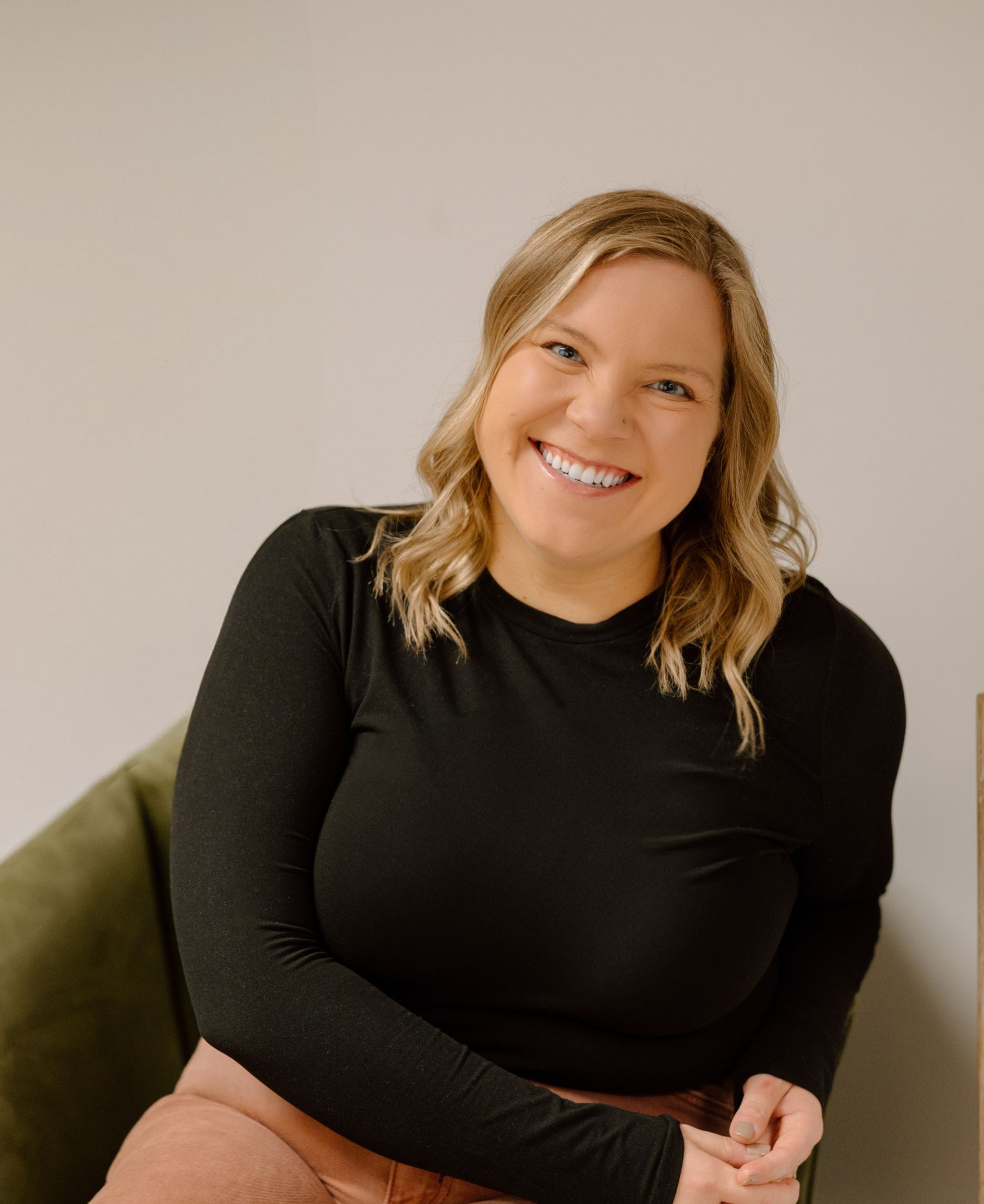 A woman is sitting in a chair wearing a black shirt and smiling.