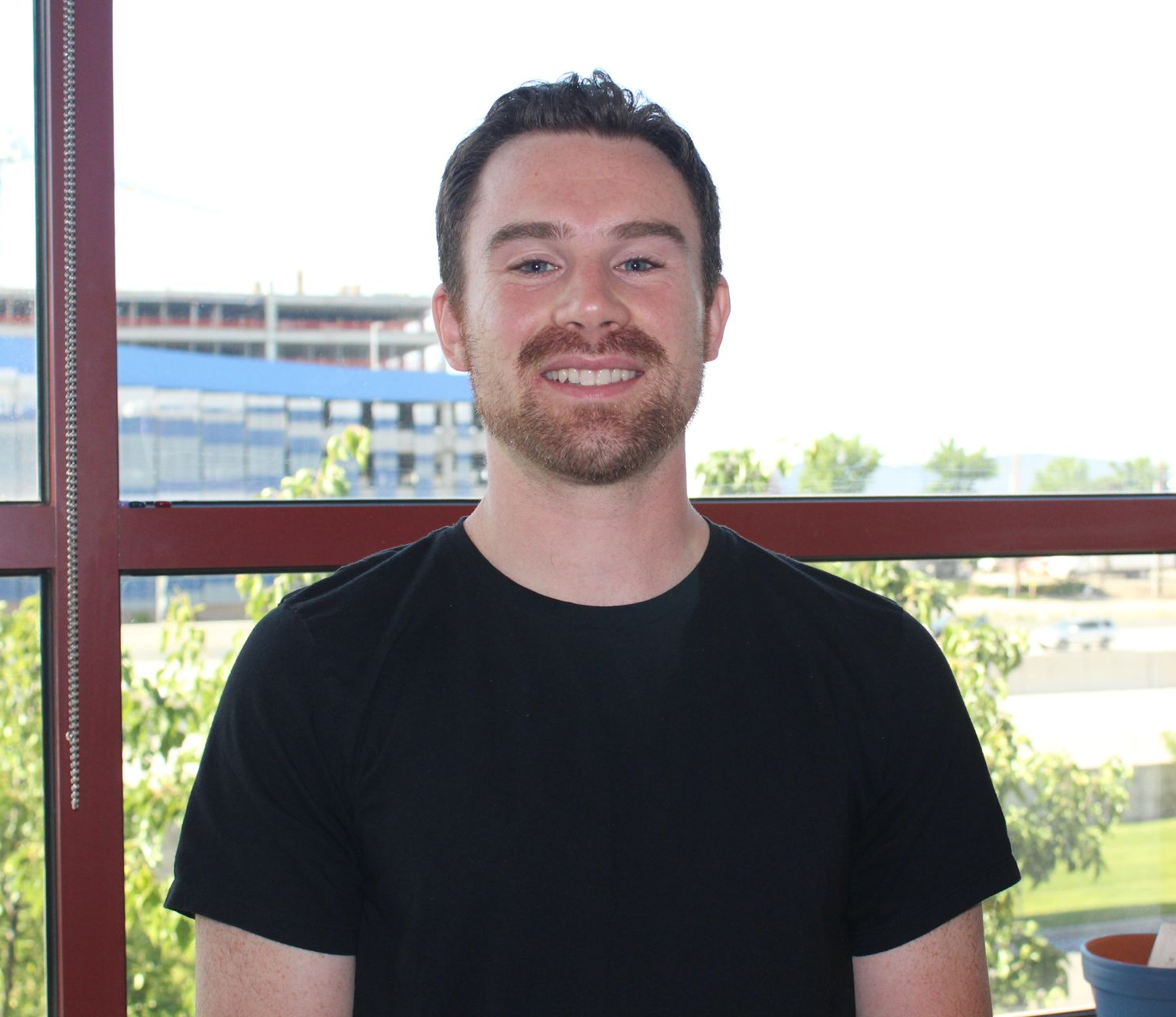 A man with a beard is wearing a purple shirt and smiling.