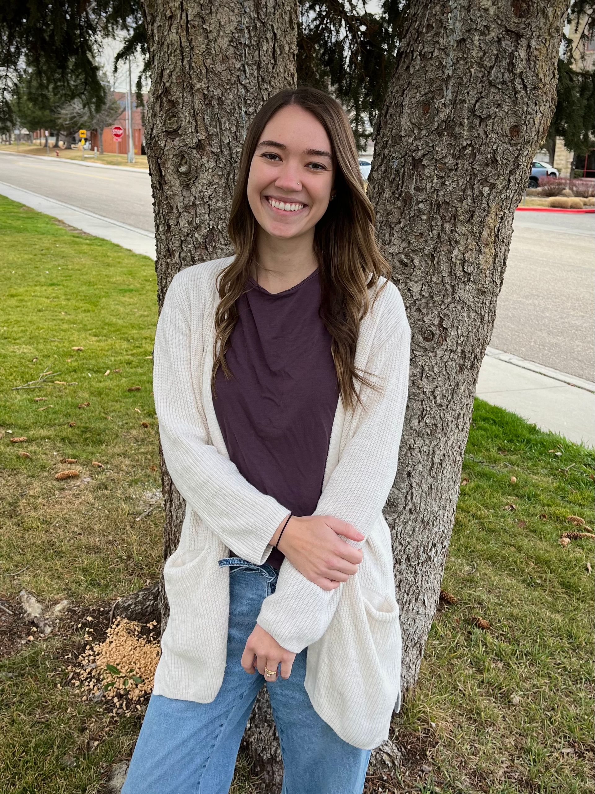 A woman in a white sweater and black shirt is smiling with her arms crossed.