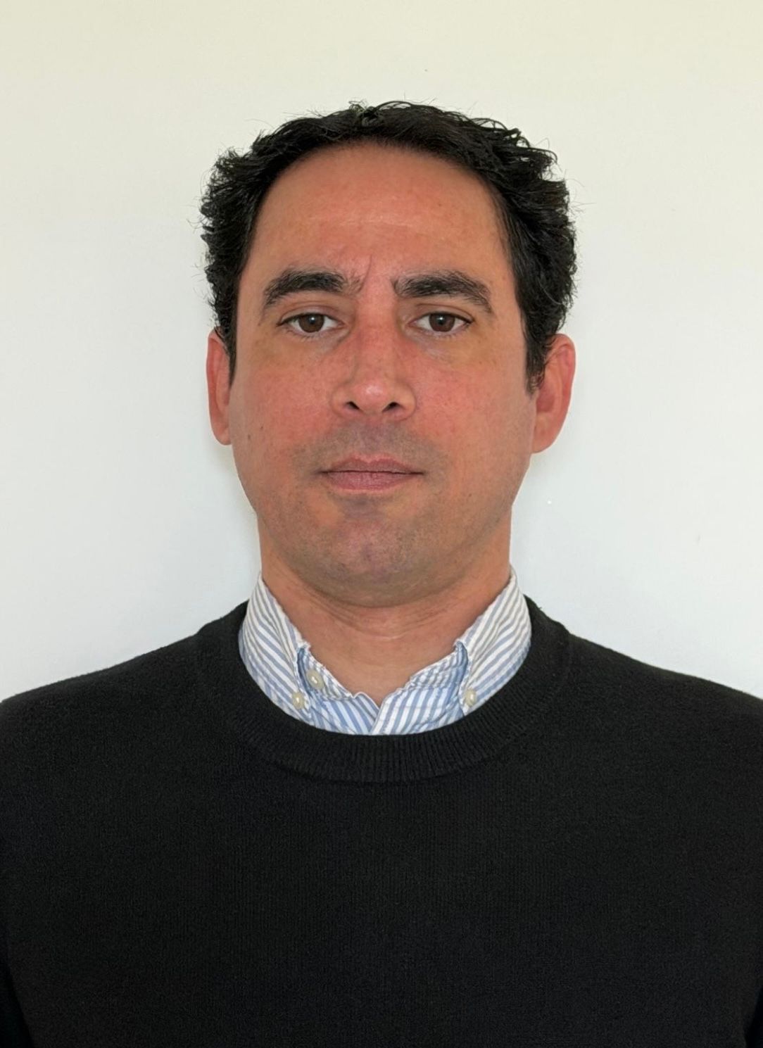 Portrait of a man in a black sweater over a striped collared shirt against a plain white background