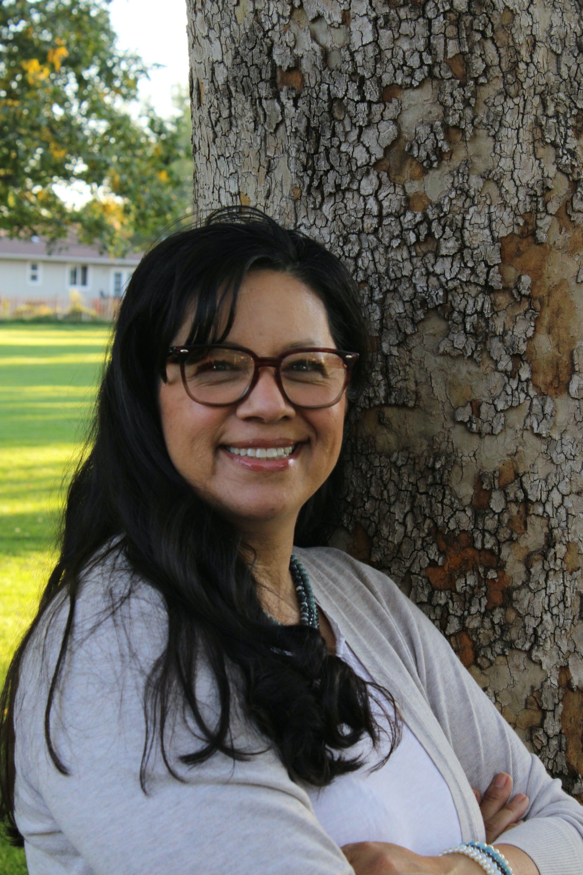 A woman in a sweater is smiling for the camera in front of a bush.