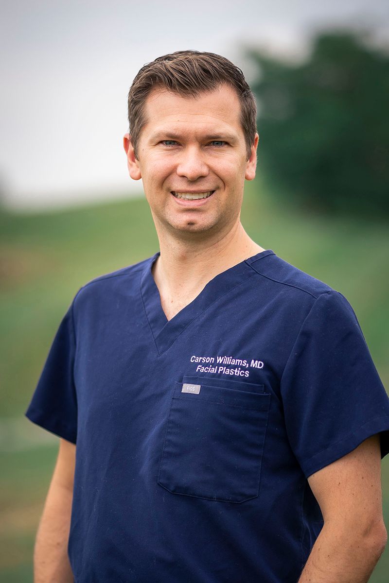 A man in a blue scrub top is standing in front of a field.