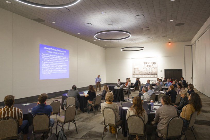 A group of people are sitting at tables in a conference room watching a presentation.