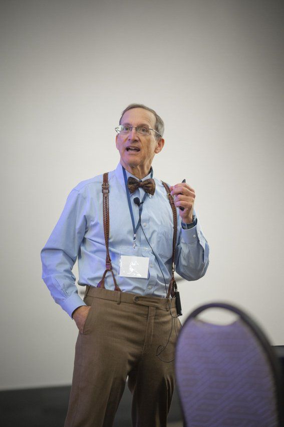 A man wearing suspenders and a bow tie is giving a presentation.