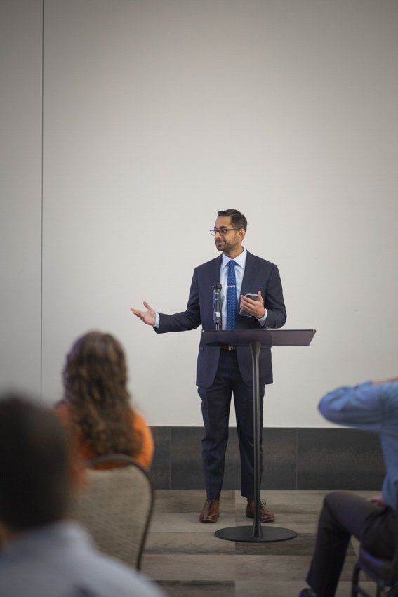 A man in a suit and tie is standing at a podium giving a presentation to a group of people.