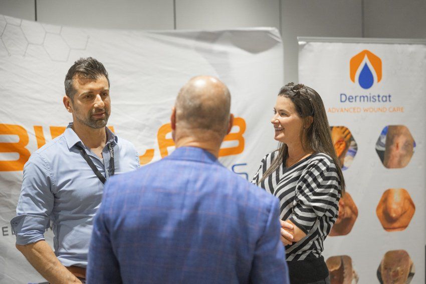 A man and a woman are talking to each other in front of a sign that says dermistot.