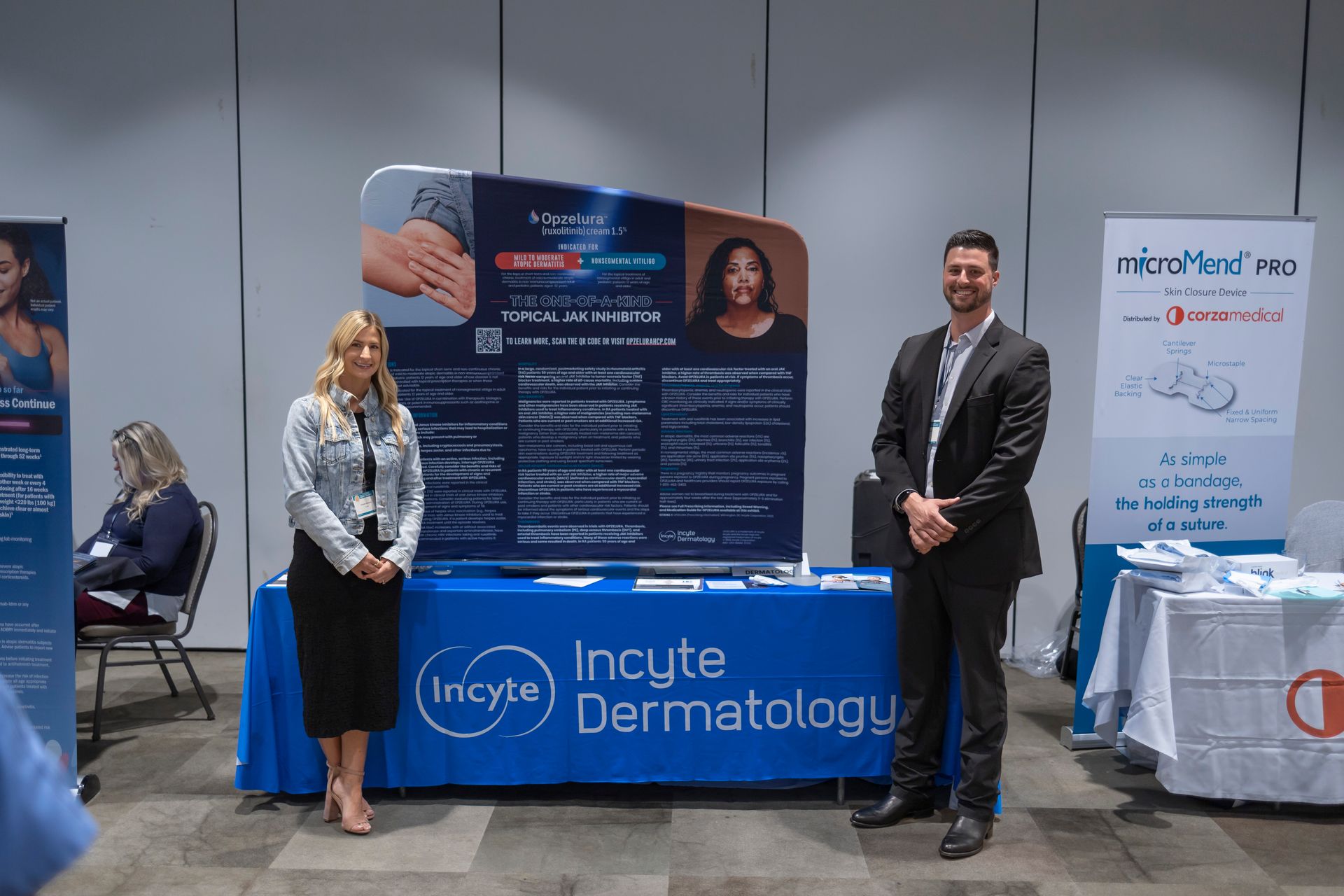 A man and a woman are standing in front of a table that says incyte dermatology.