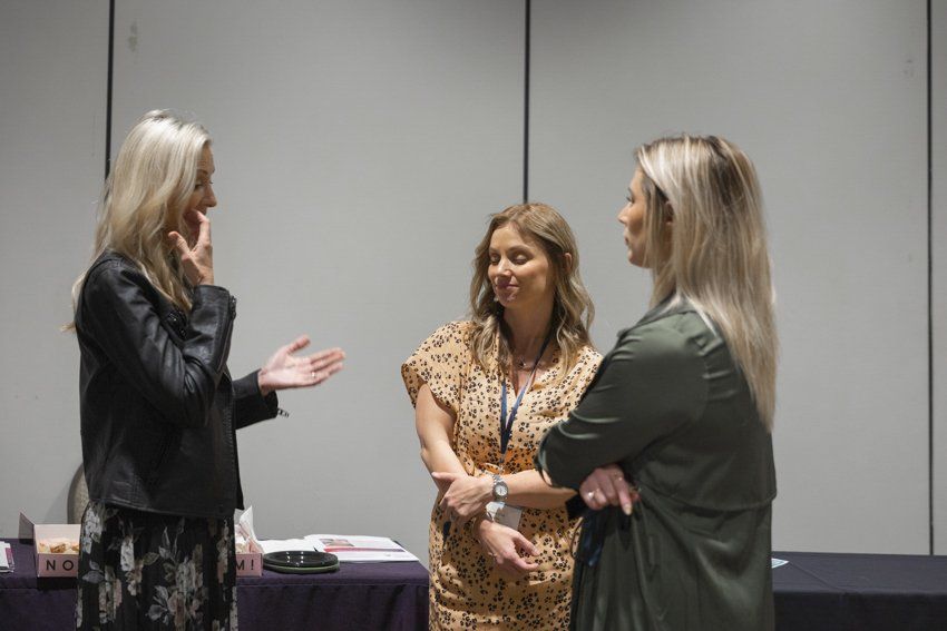 Three women are standing next to each other in a room talking to each other.