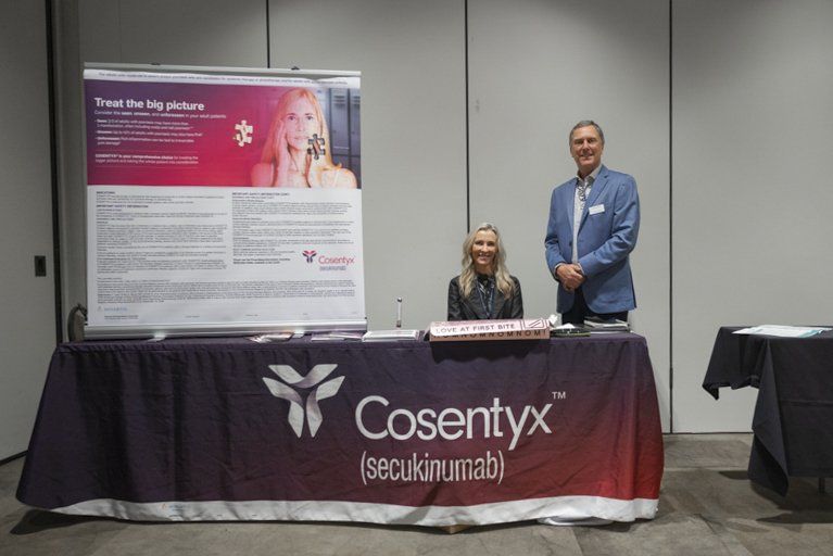 Two people standing behind a table with a cosentyx sign on it