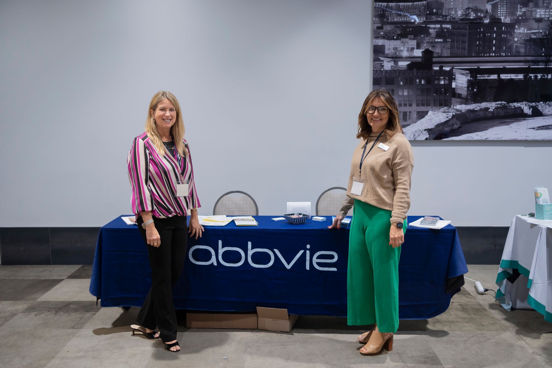 Two women are standing in front of a table that says abbvie on it.