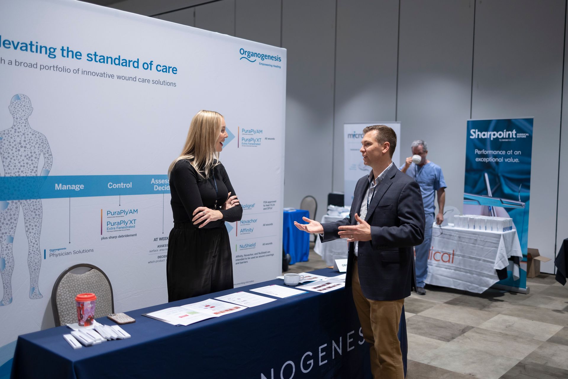 A man and a woman are standing at a table talking to each other.