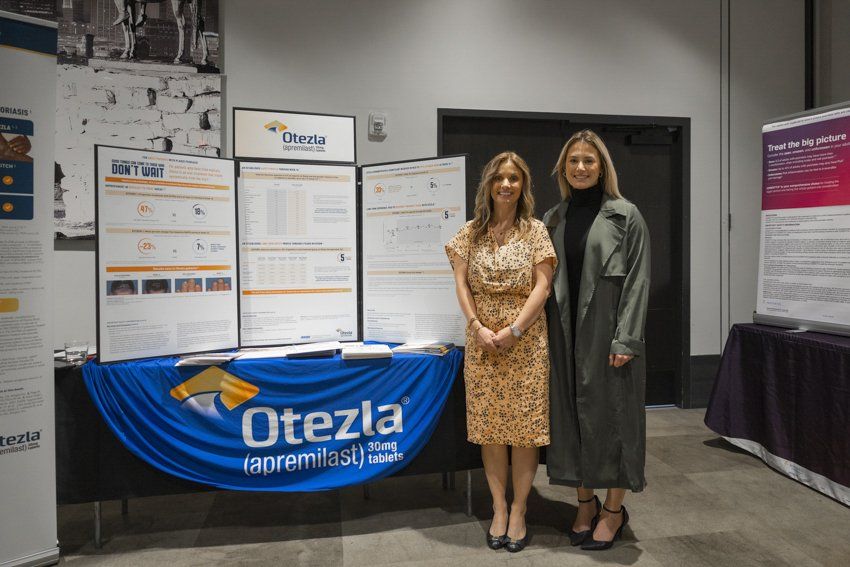 Two women are standing in front of a table with posters on it.