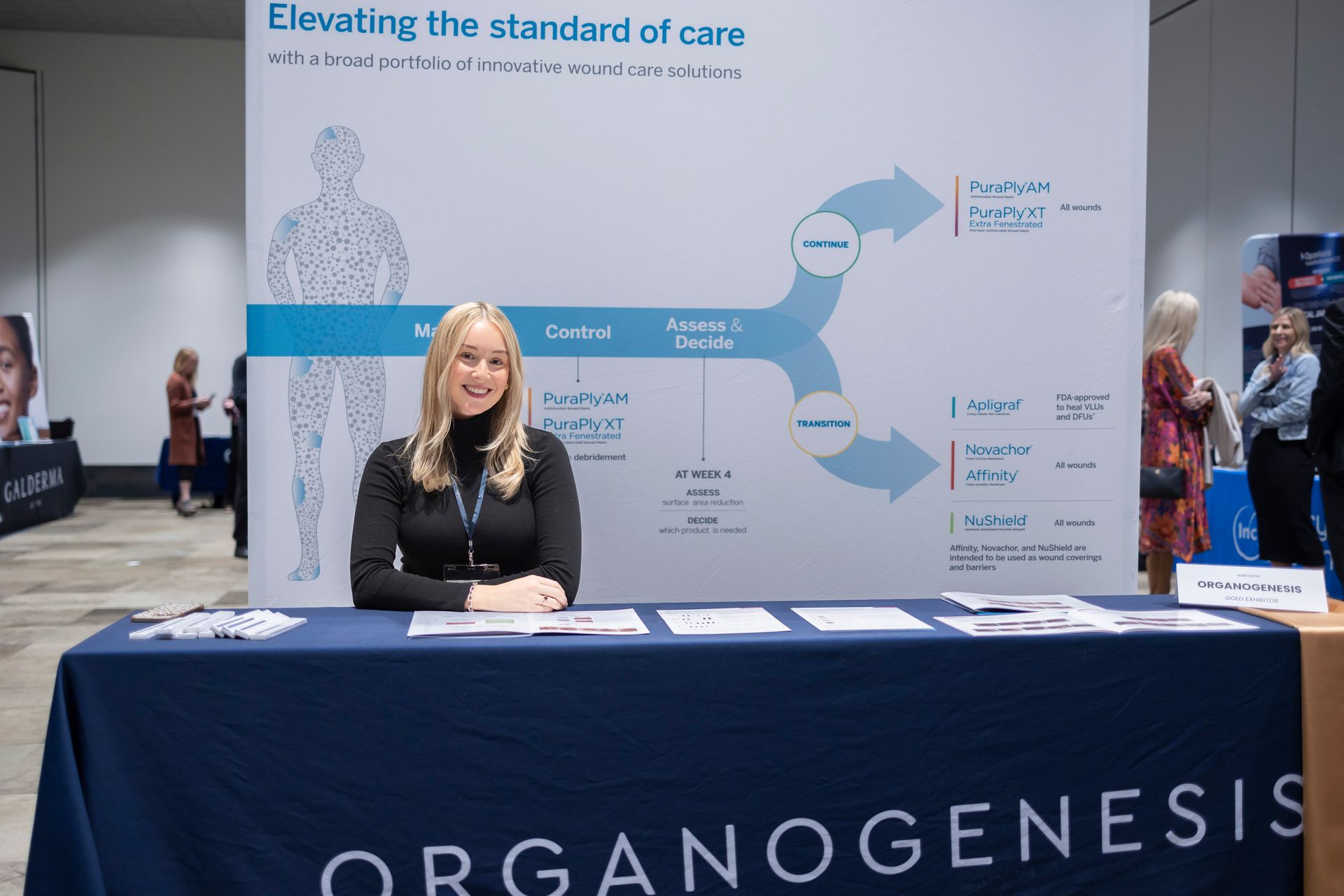 A woman is sitting at a table in front of a sign that says organogenesis
