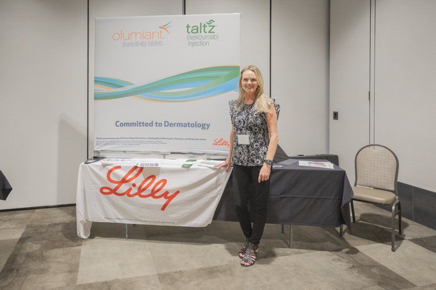 A woman stands in front of a table with a lilly banner on it