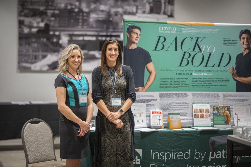 Two women are standing in front of a table with a sign that says back to bold.