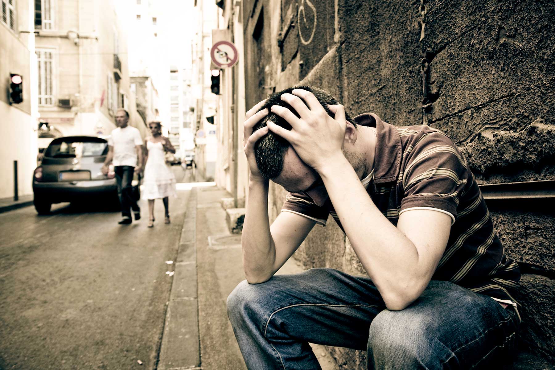 Man Sitting on the Street and Holding His Head — Portage, MI — Cornerstone Chiropractic Center