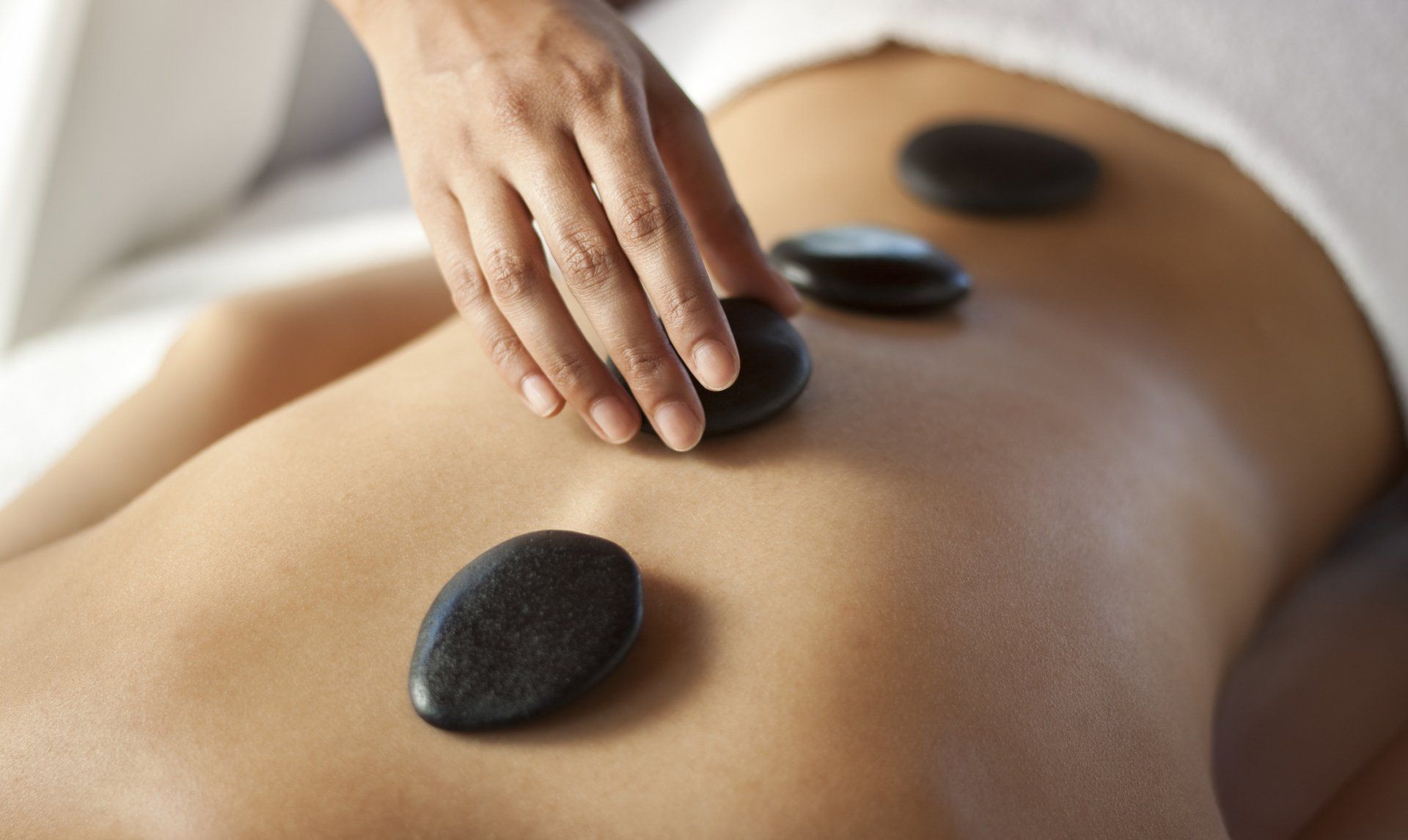 Person receiving a hot stone massage; dark stones on their back, hand placing one.