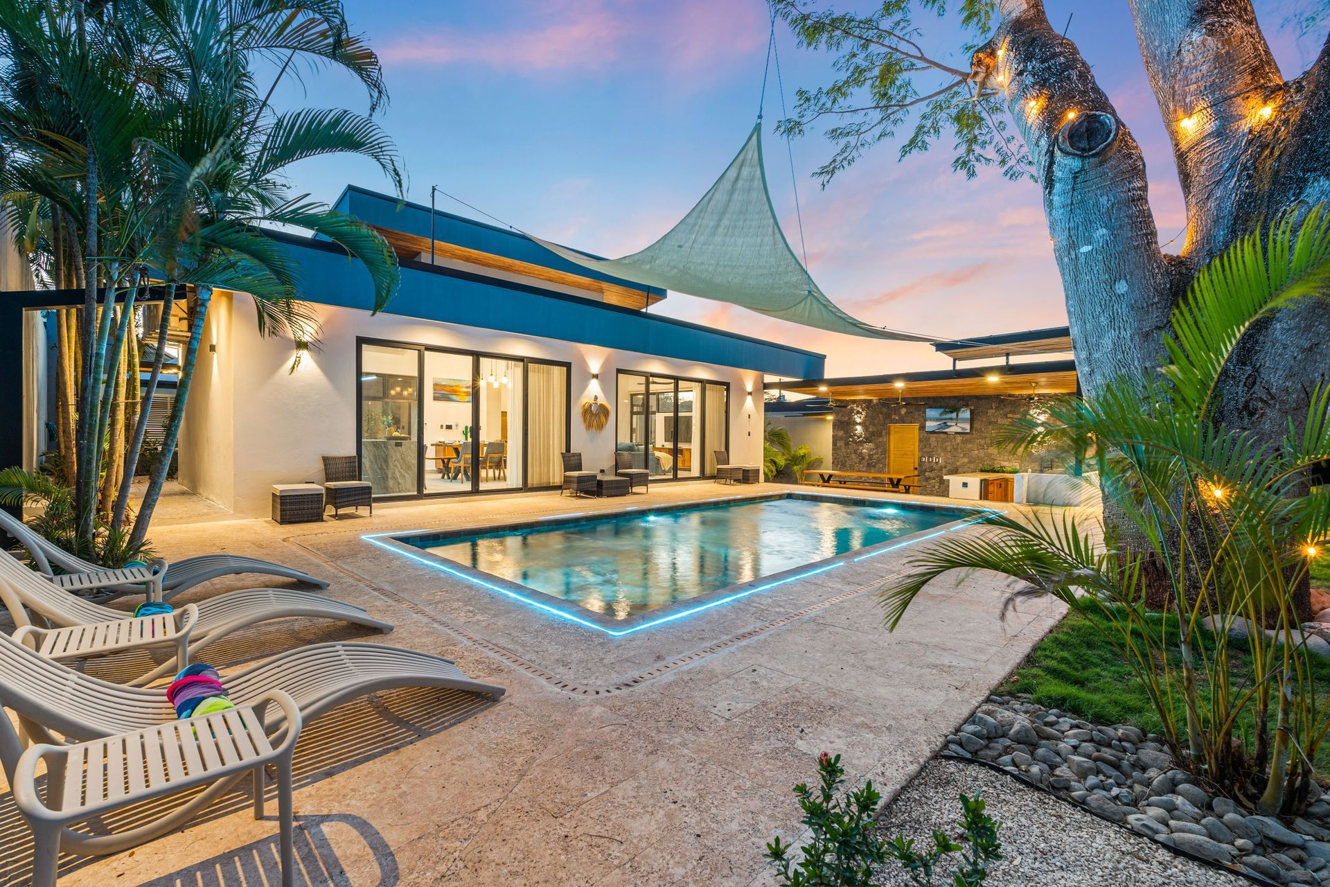 Luxury home exterior with pool and lounge chairs at dusk.