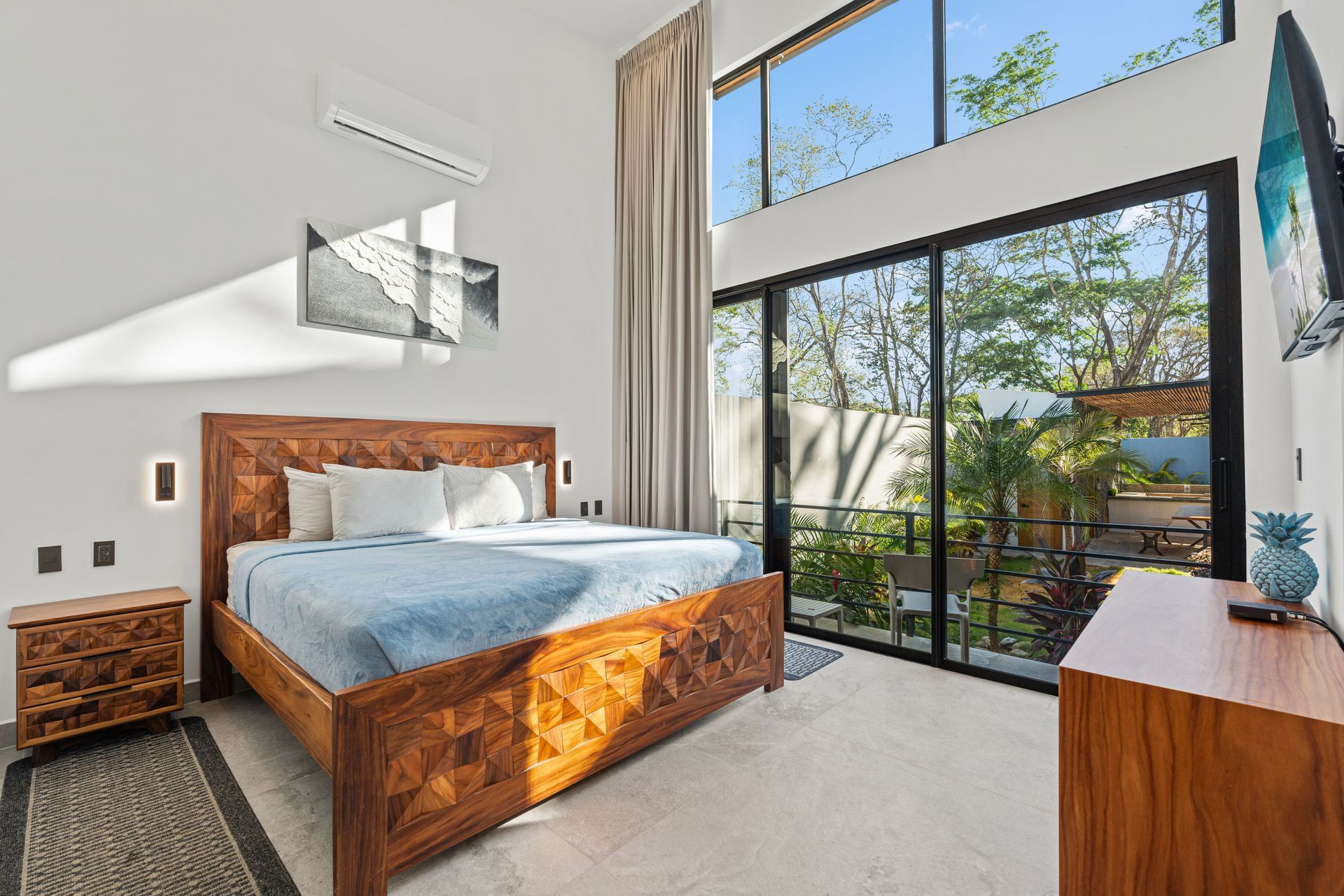 Bedroom with wooden furniture, a large window overlooking a garden, and a mounted TV.